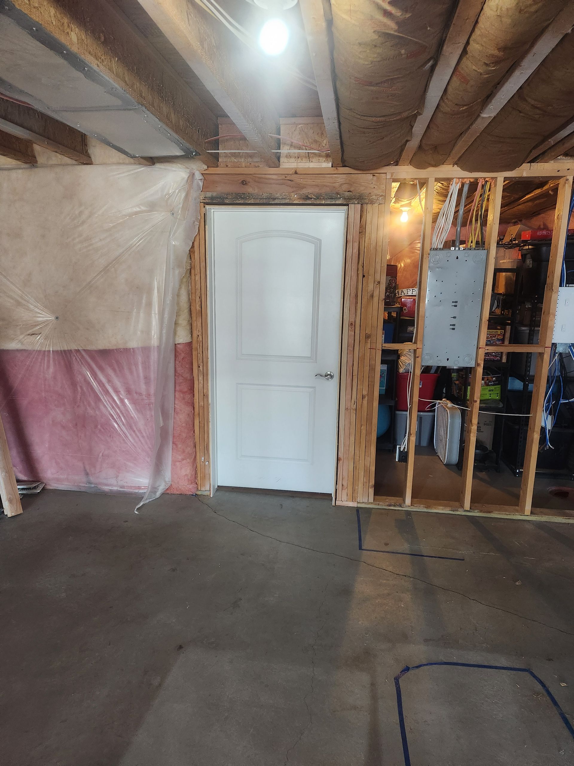 Basement interior with white door, exposed beams, pink lower wall, and unfinished storage area.