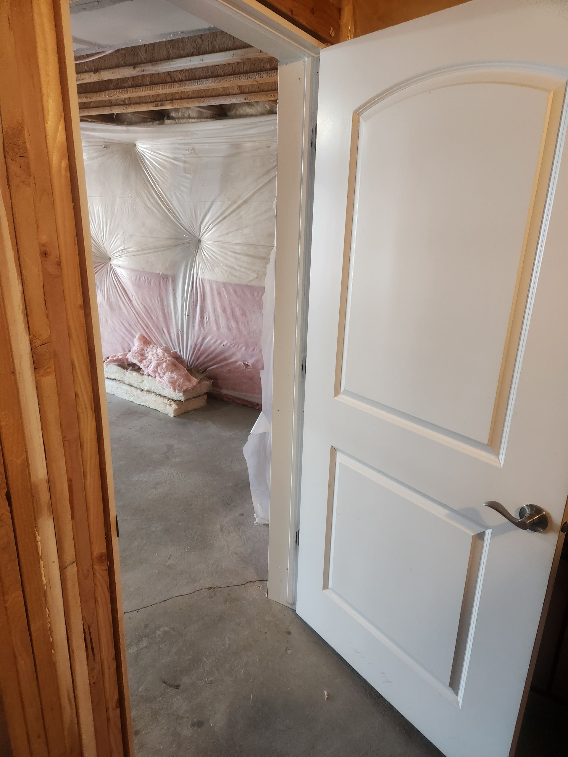 Partially open white door leading to a room under construction with insulation exposed on the walls