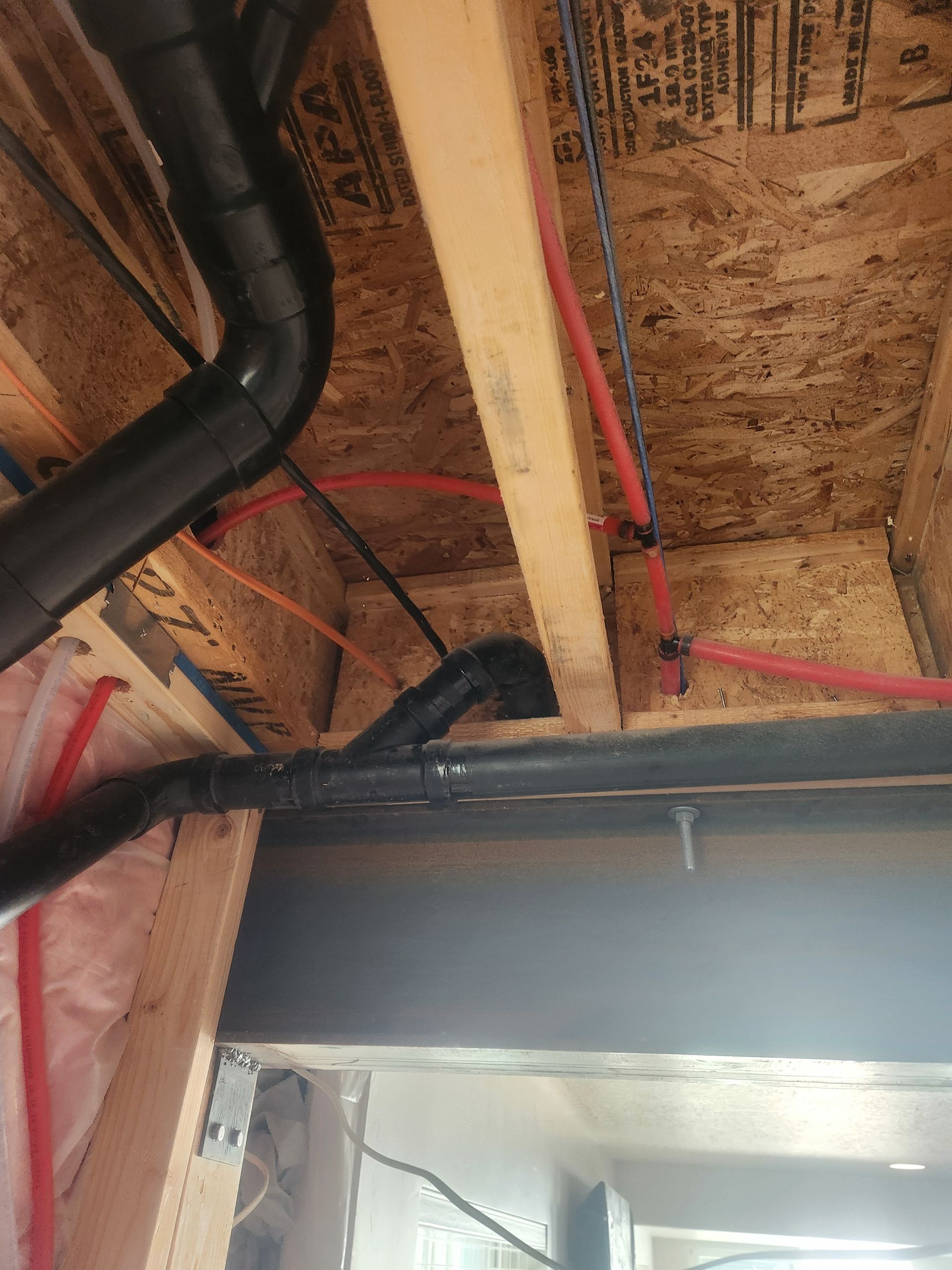 Exposed attic framing with black ducting, red wiring, and a gray garage door header below