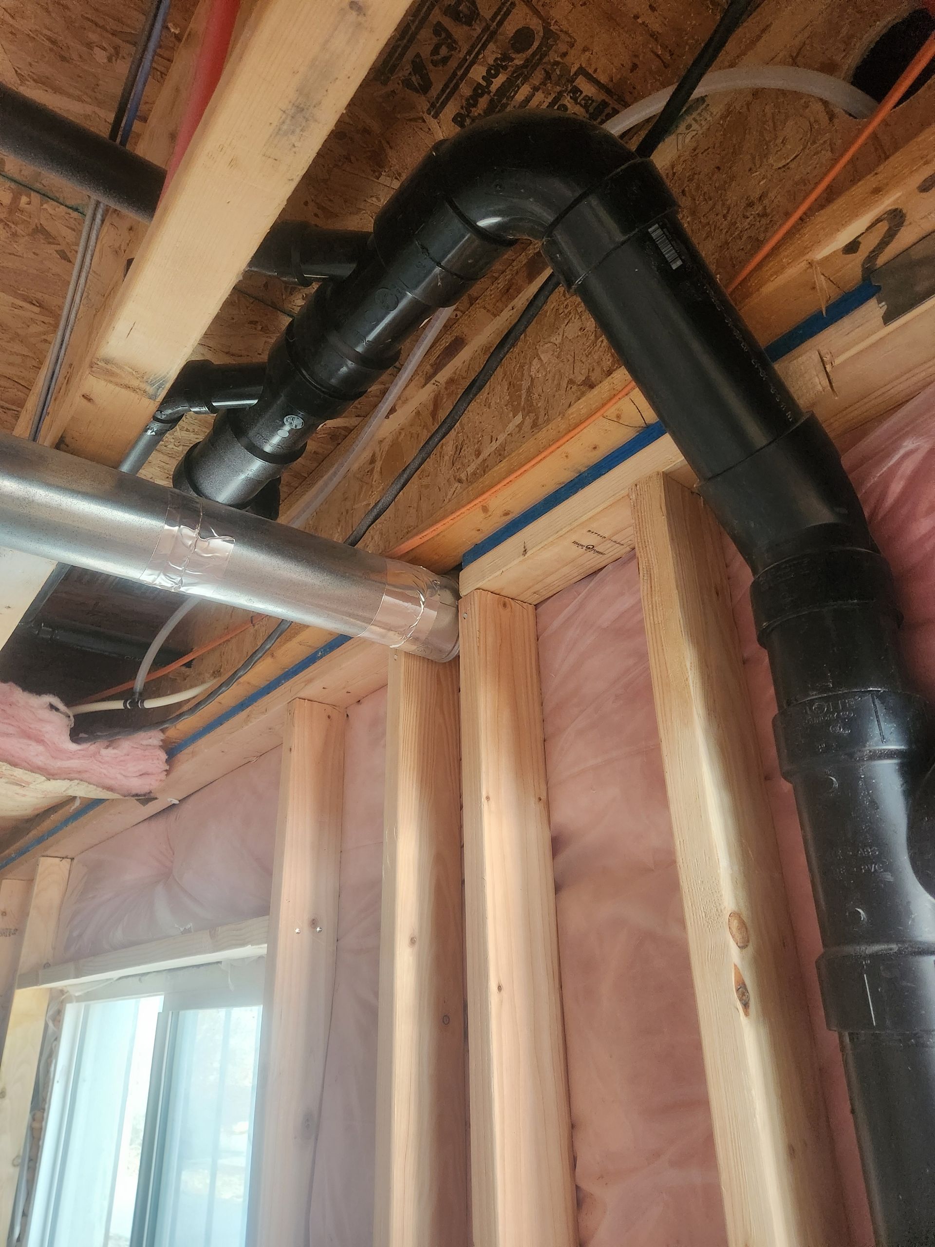 Exposed black HVAC ducting and a silver pipe running through unfinished attic framing and insulation.