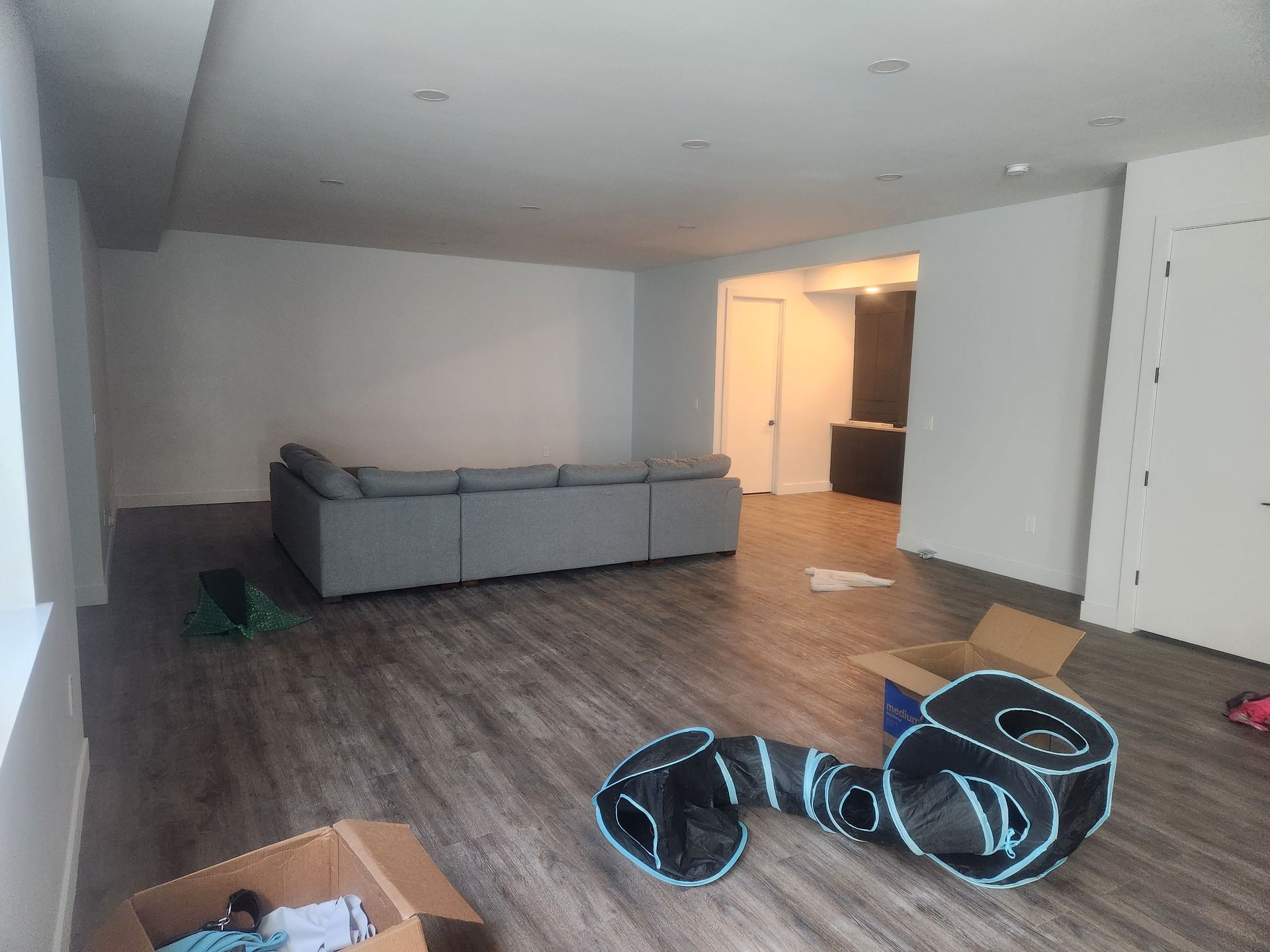 Empty living room with gray sofa, wood floors, and a glowing hallway doorway; inflatable pool float on floor