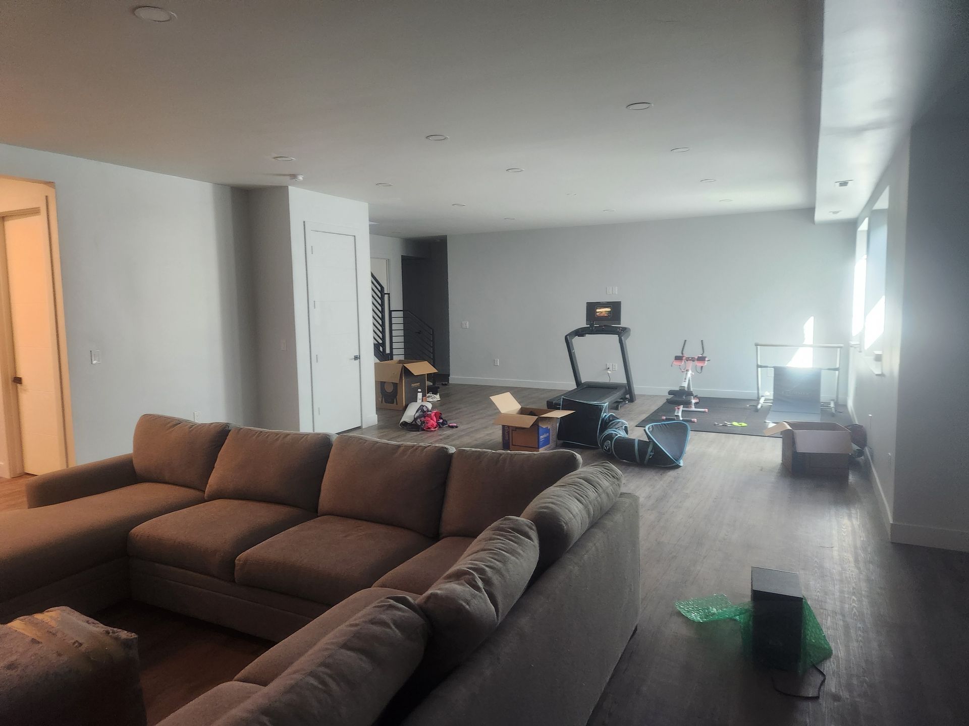Spacious living room with a brown sectional sofa and scattered exercise equipment on the floor