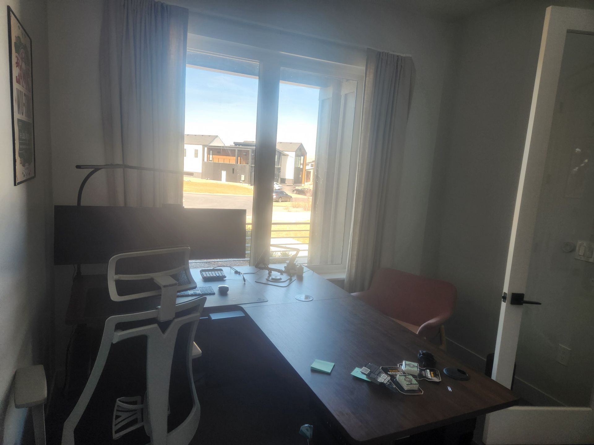 Home office with a desk, computer chair, and open curtains facing a bright outdoor view.