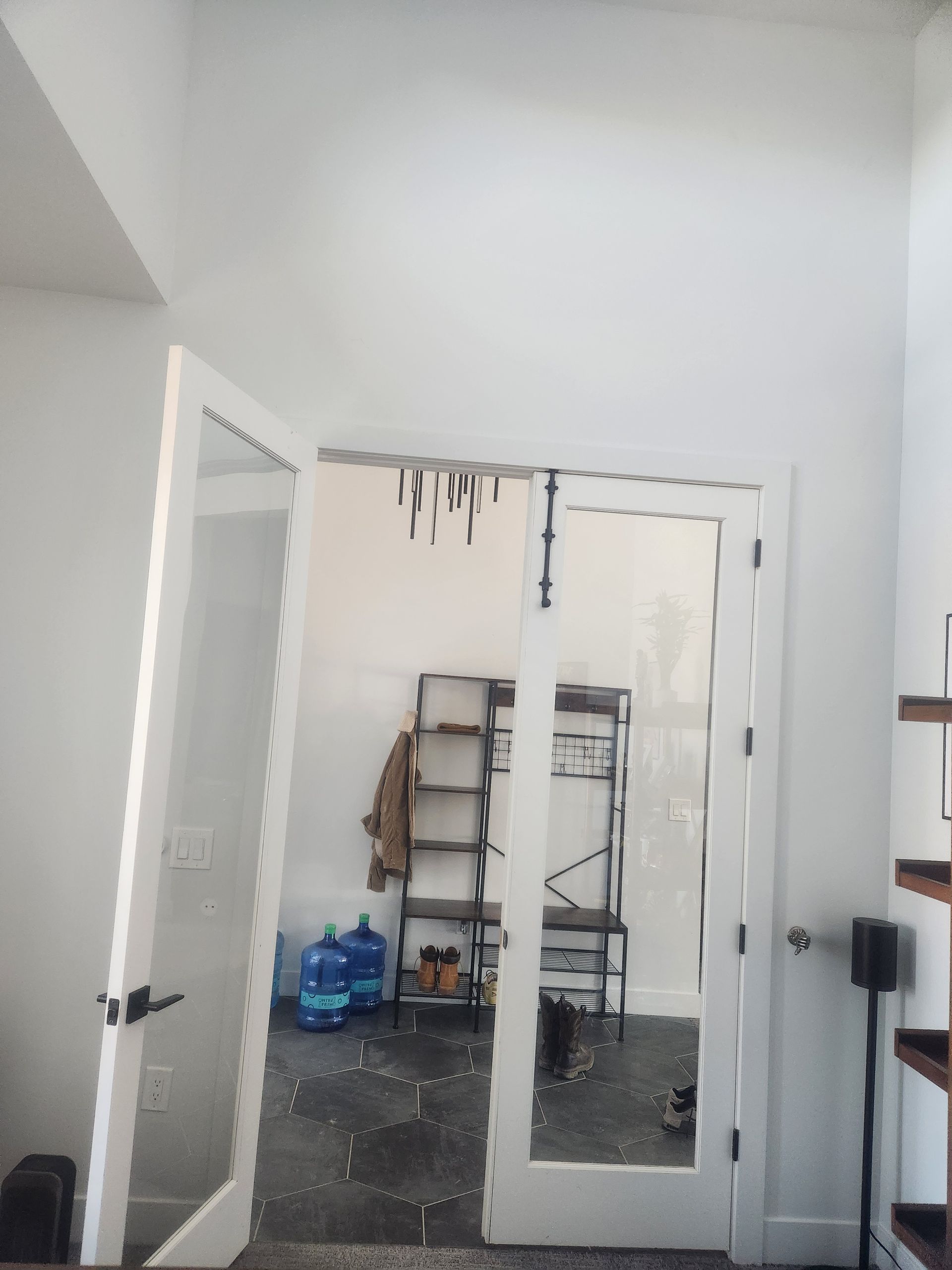 Open white double doors to a small cluttered room with a ladder, buckets, and tools inside.