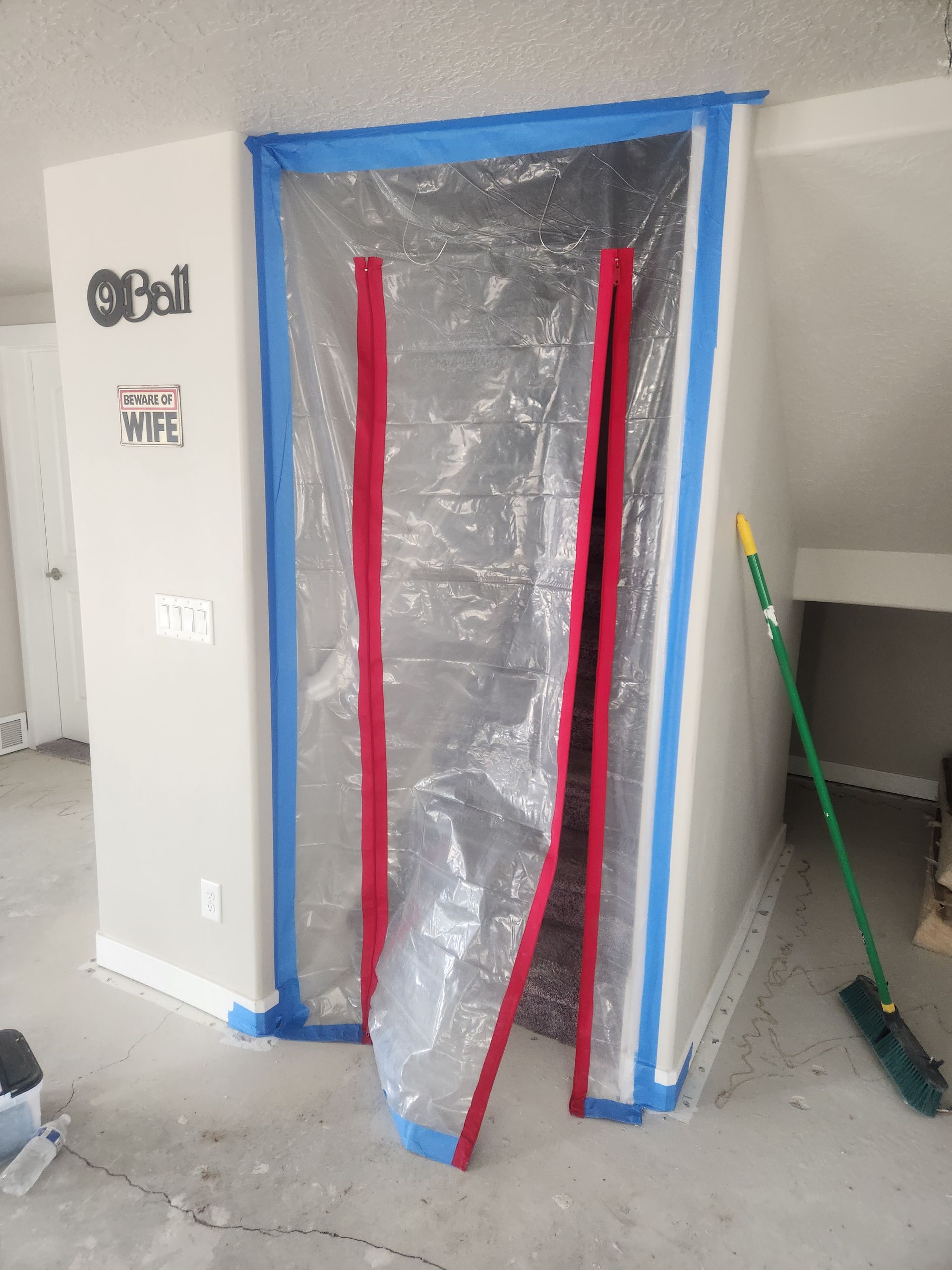 Doorway covered in plastic sheeting and blue tape, with red strips hanging down in a room under renovation