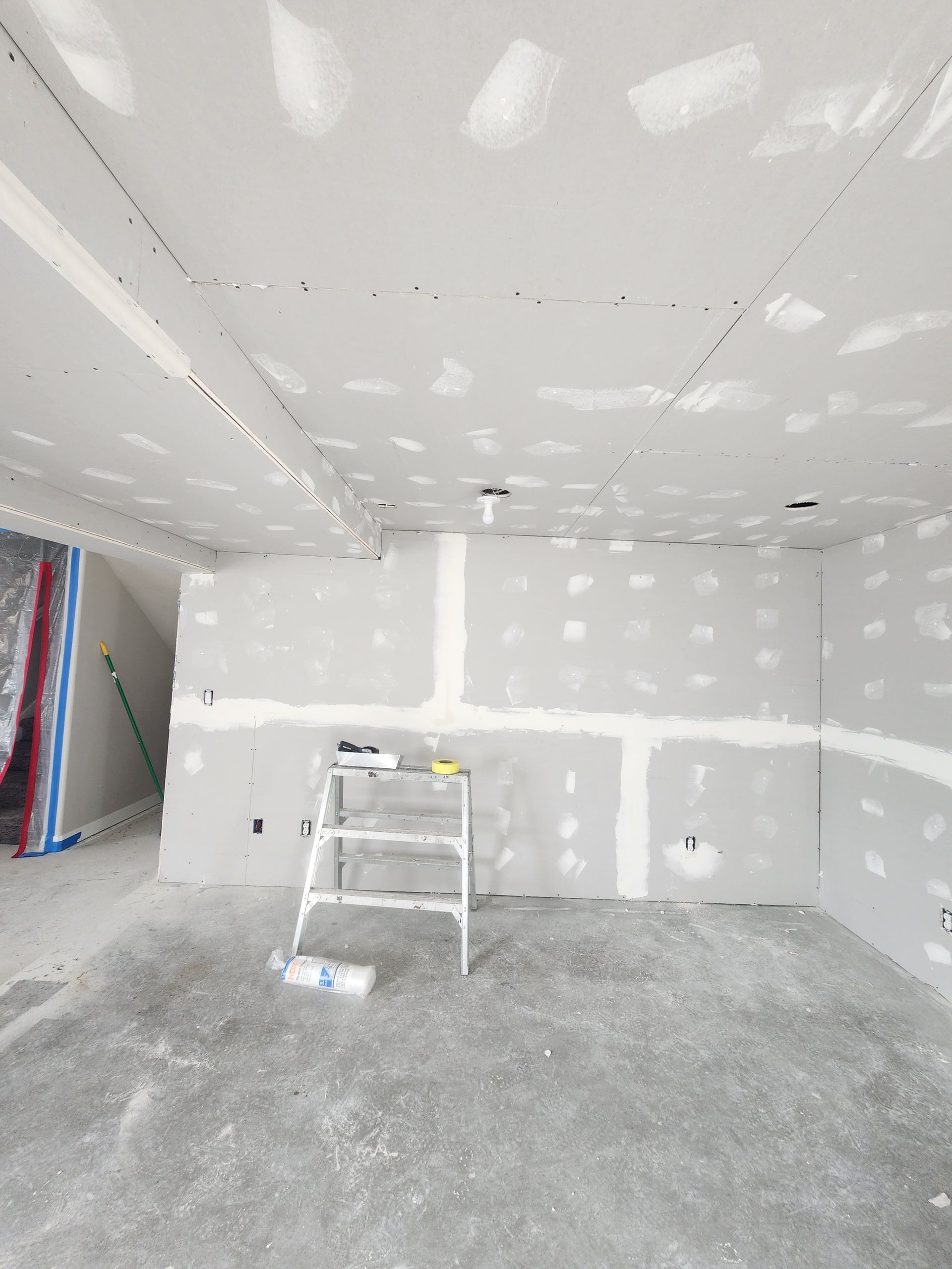 Unfinished room with drywall patches, a ladder, and concrete floor under construction.