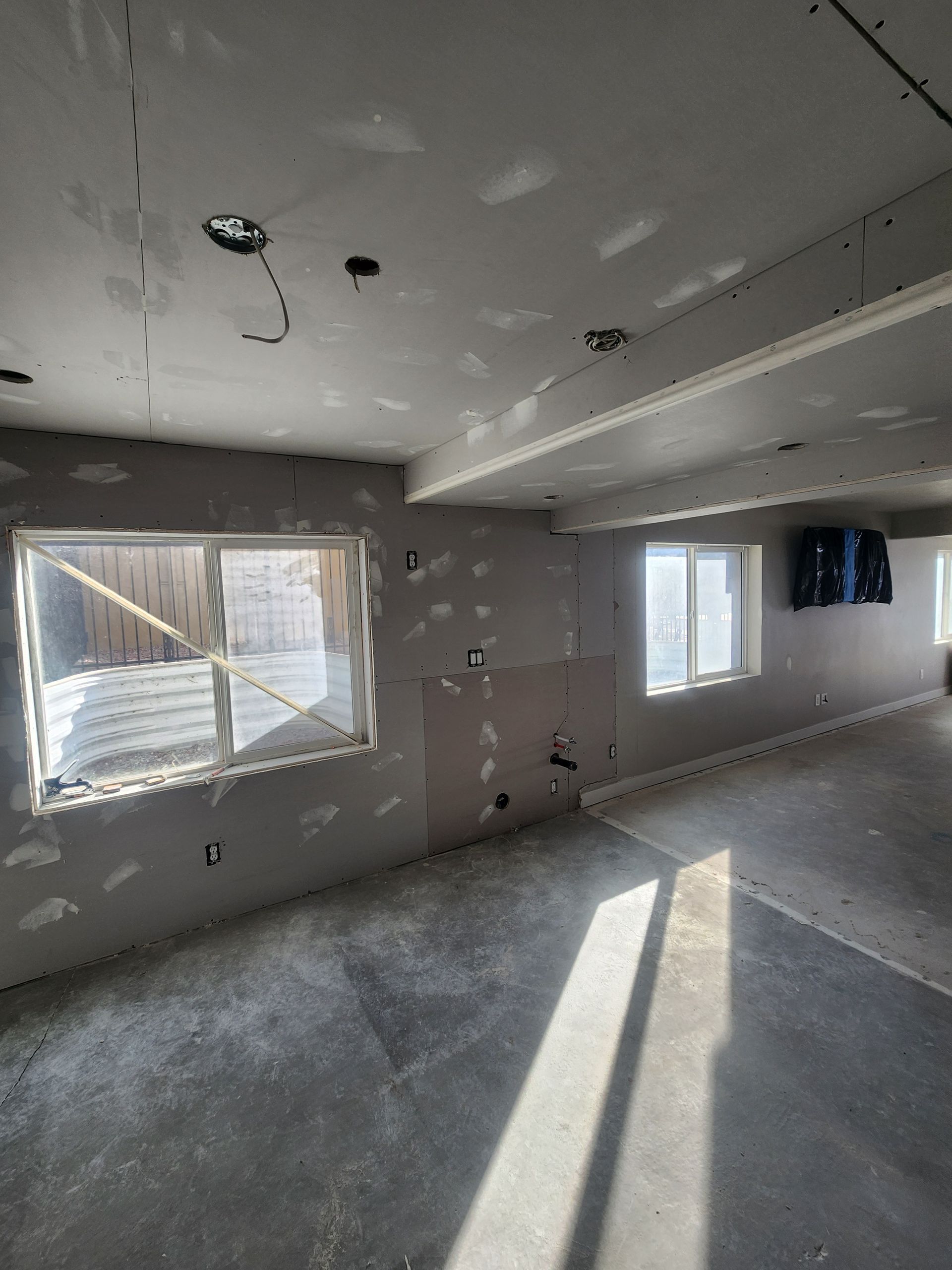 Empty unfinished room with gray walls, carpet, windows, and sunlight streaming across the floor