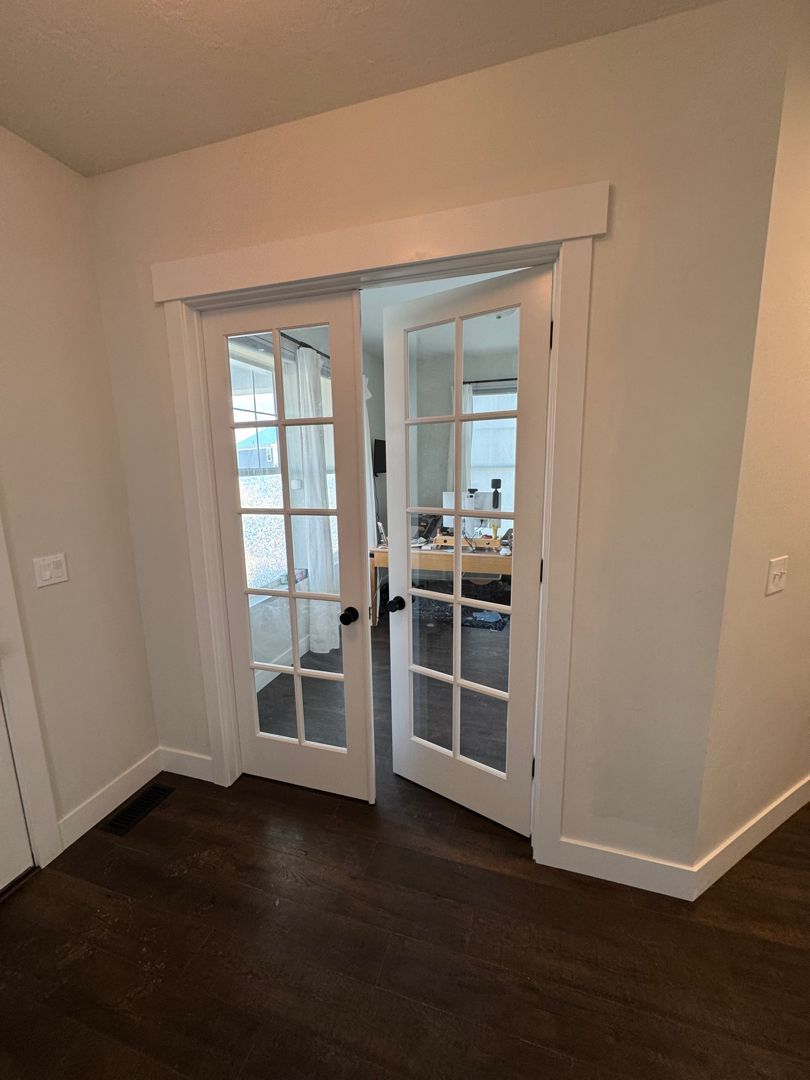 Empty room with dark wood floors and white French doors opening to a bright adjacent space