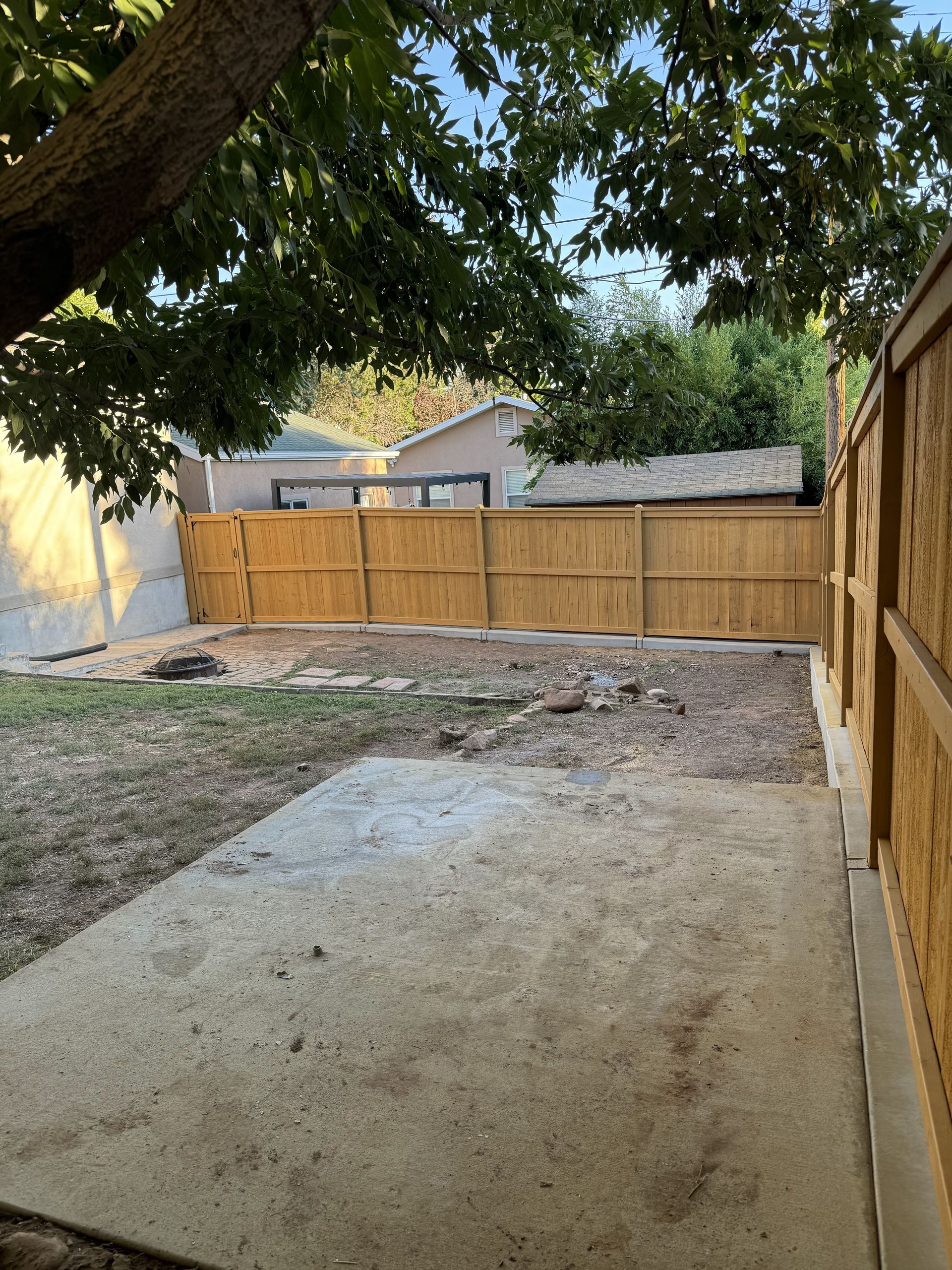 Backyard patio with concrete slab, tree overhead, and wooden fence at the back and right side