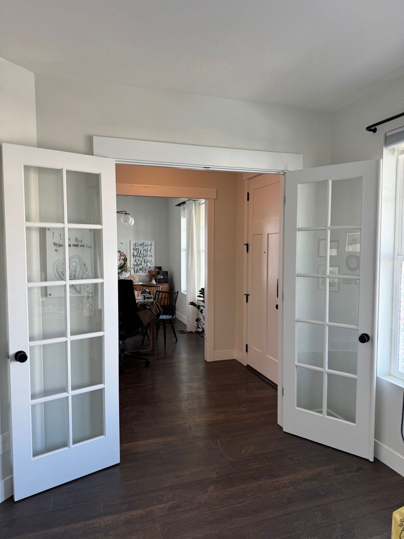 Open French doors leading from a dark wood-floored hallway into a softly lit room.