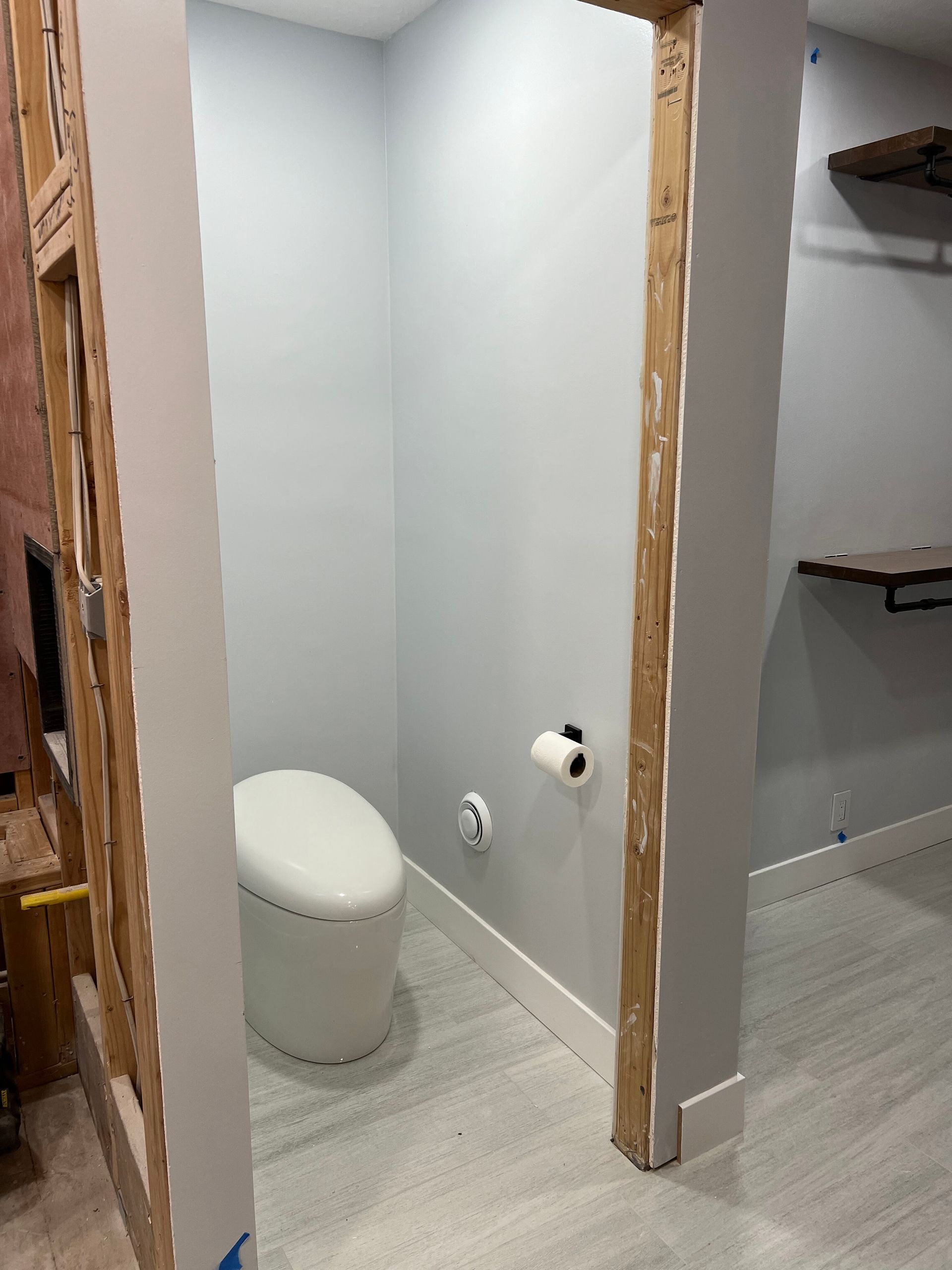 Small unfinished bathroom with toilet, toilet paper holder, and shelves on the right.