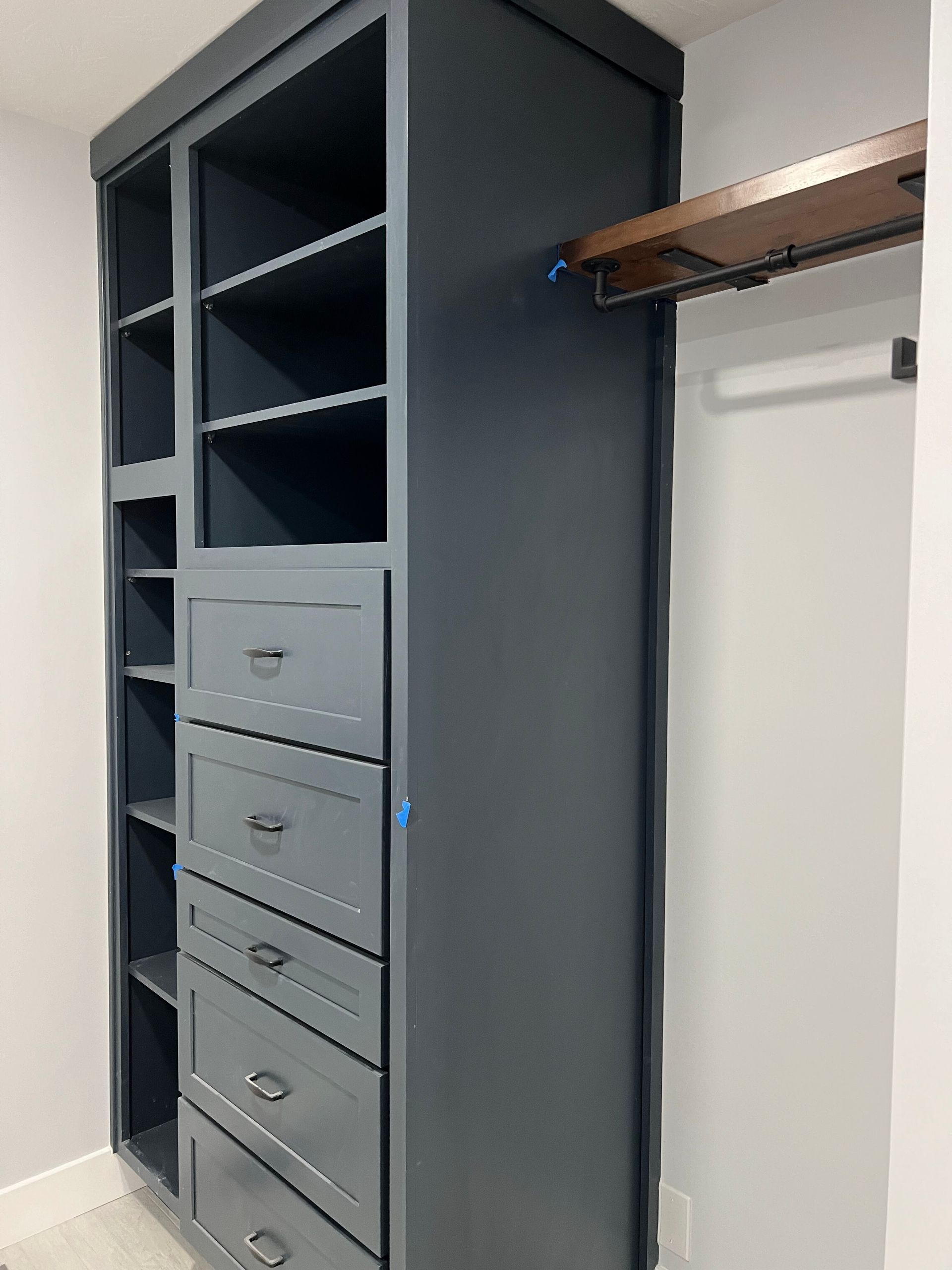 Built-in dark gray closet with open shelving, drawers, and a hanging rod in a hallway.