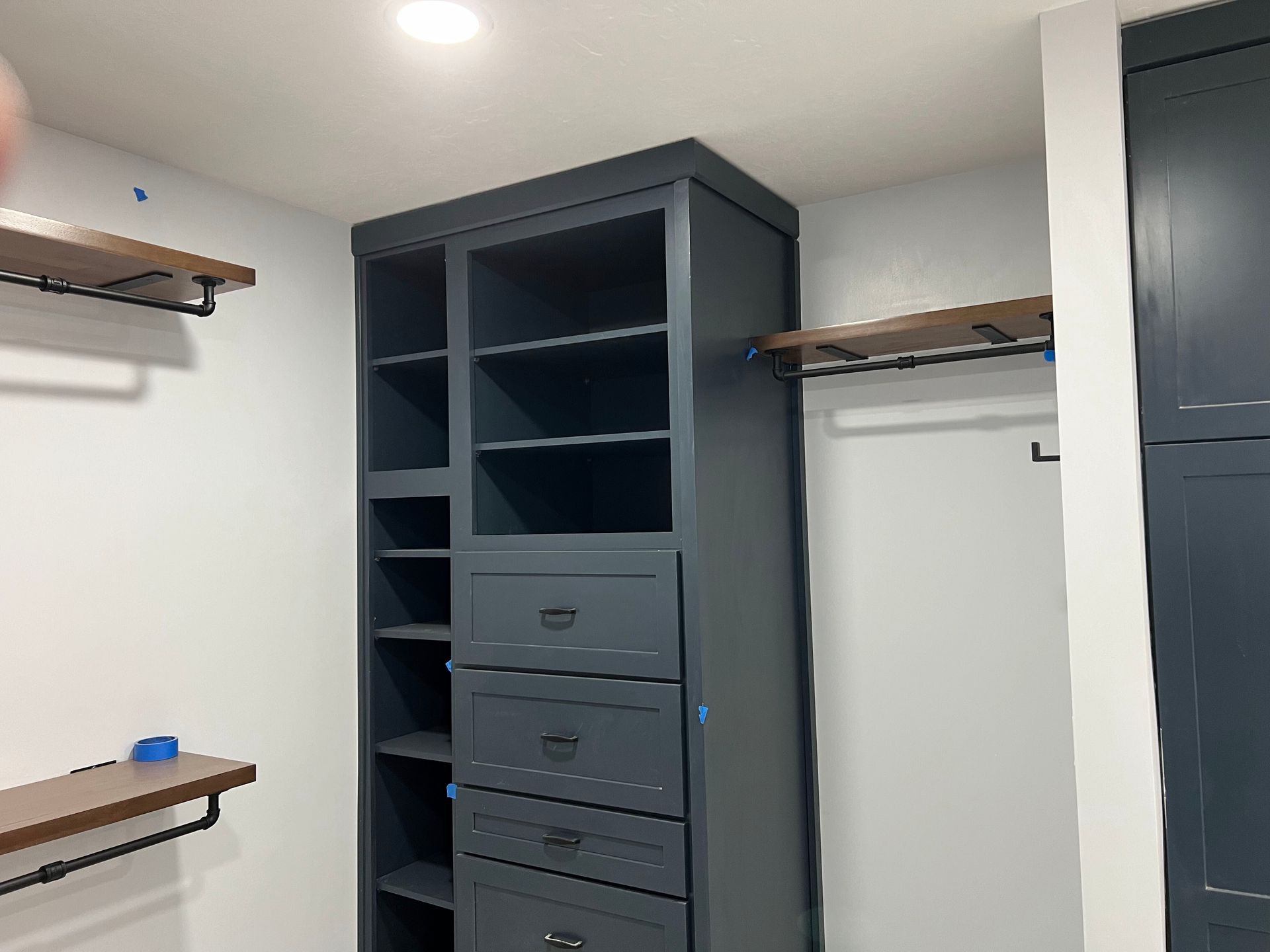 Empty walk-in closet with dark shelving and drawers, hanging rods on both sides, and a white ceiling light.