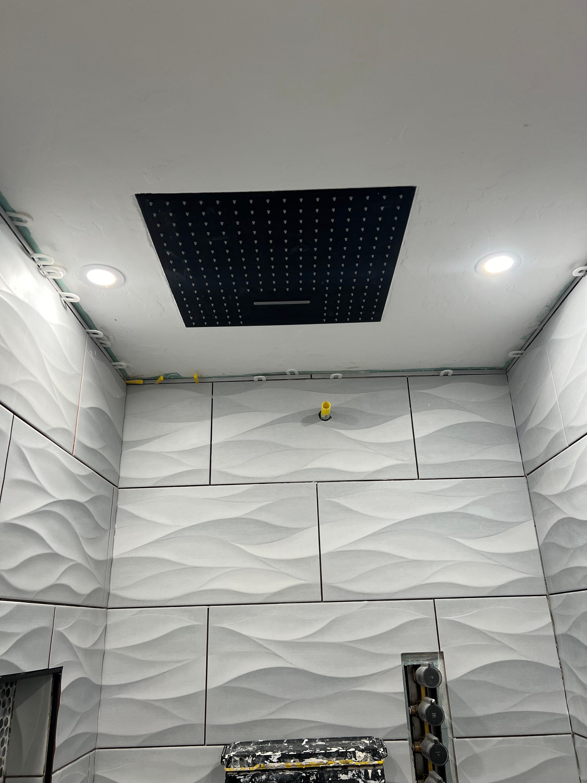 White-tiled room with a black ceiling panel and recessed lights, seen from below