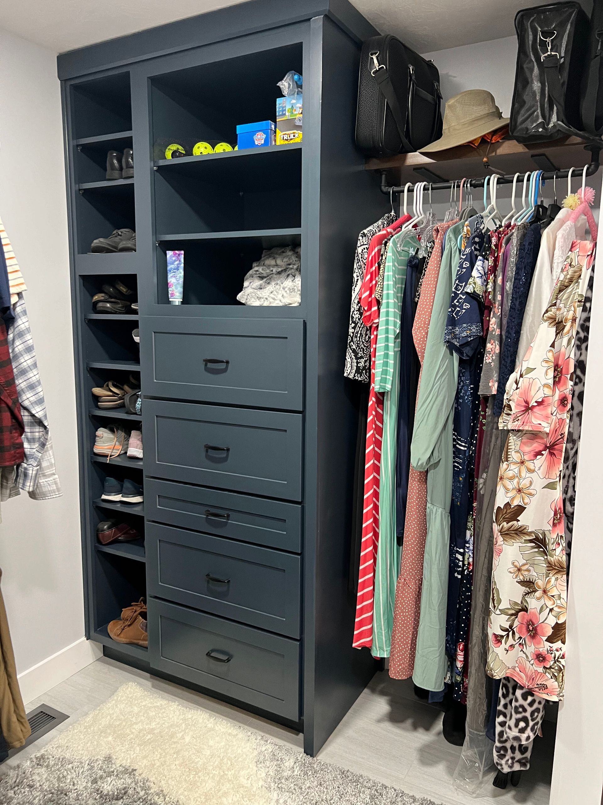 Open closet with hanging clothes, stacked drawers, shelves, shoes, and handbags in a bedroom.