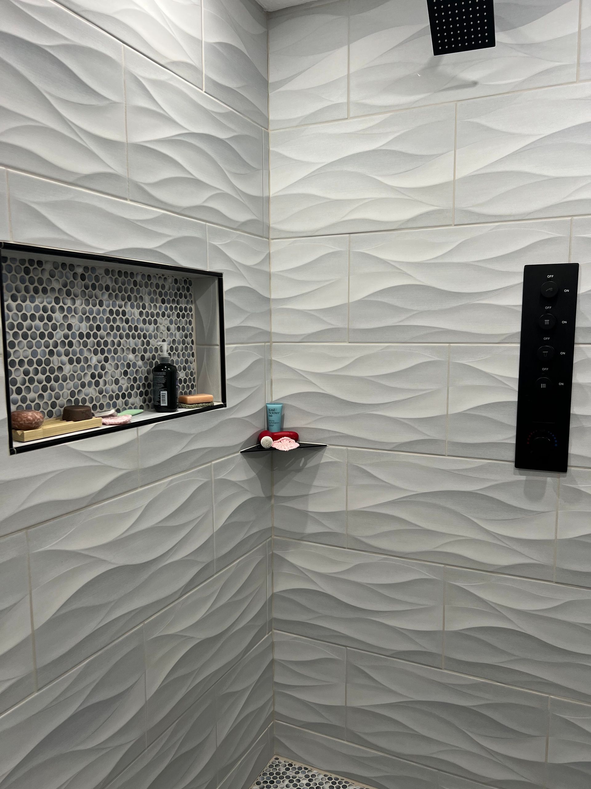 Modern bathroom shower with white textured tile walls, a niche shelf, and black fixtures