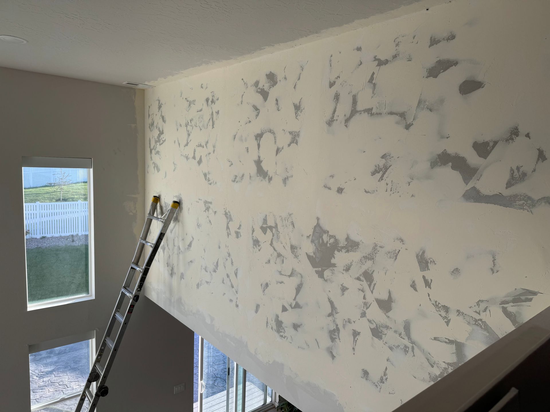 Room under renovation with ladder and patchy plaster on the wall near a window