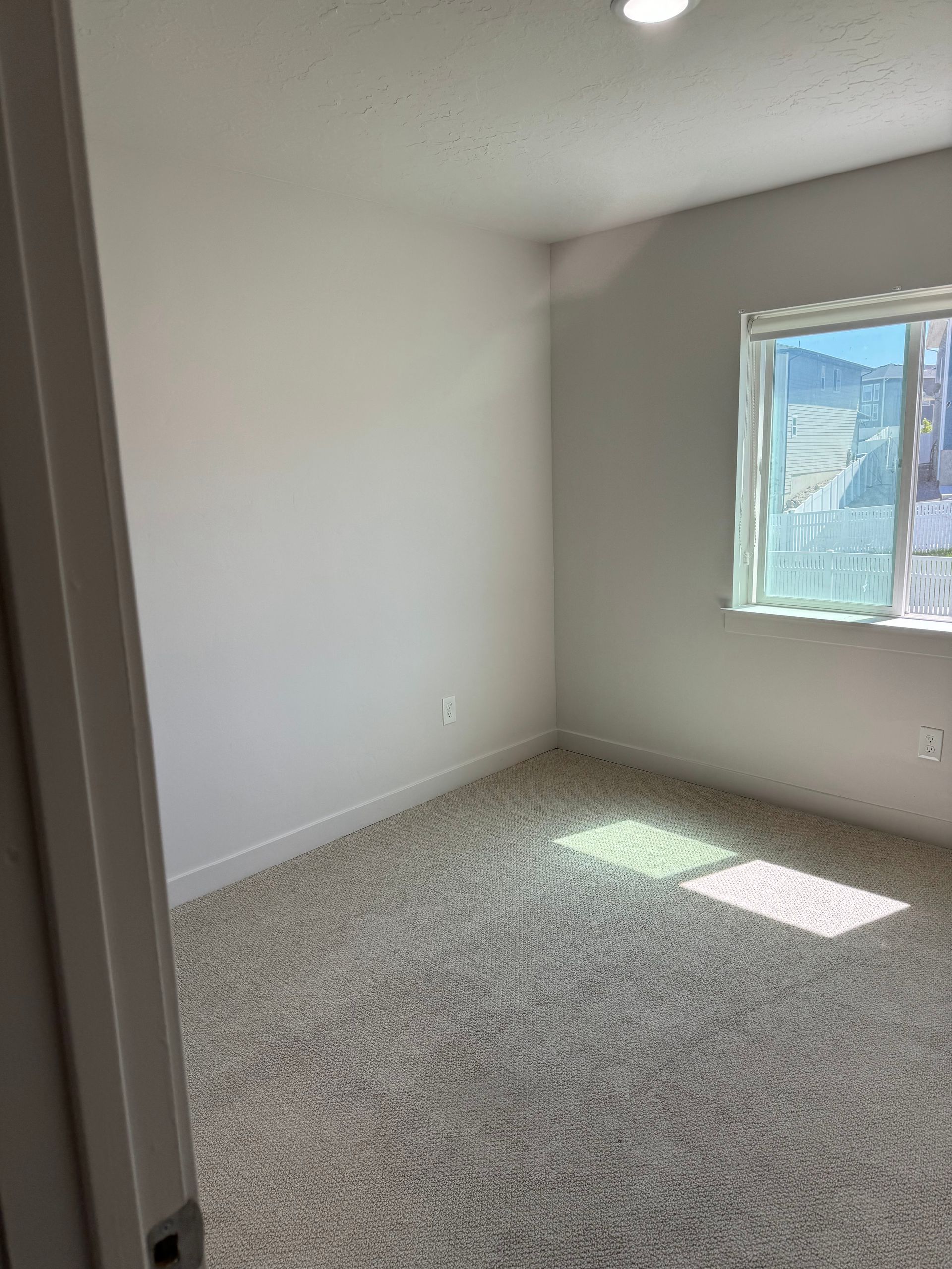 Empty carpeted room with white walls and a sunlit window.