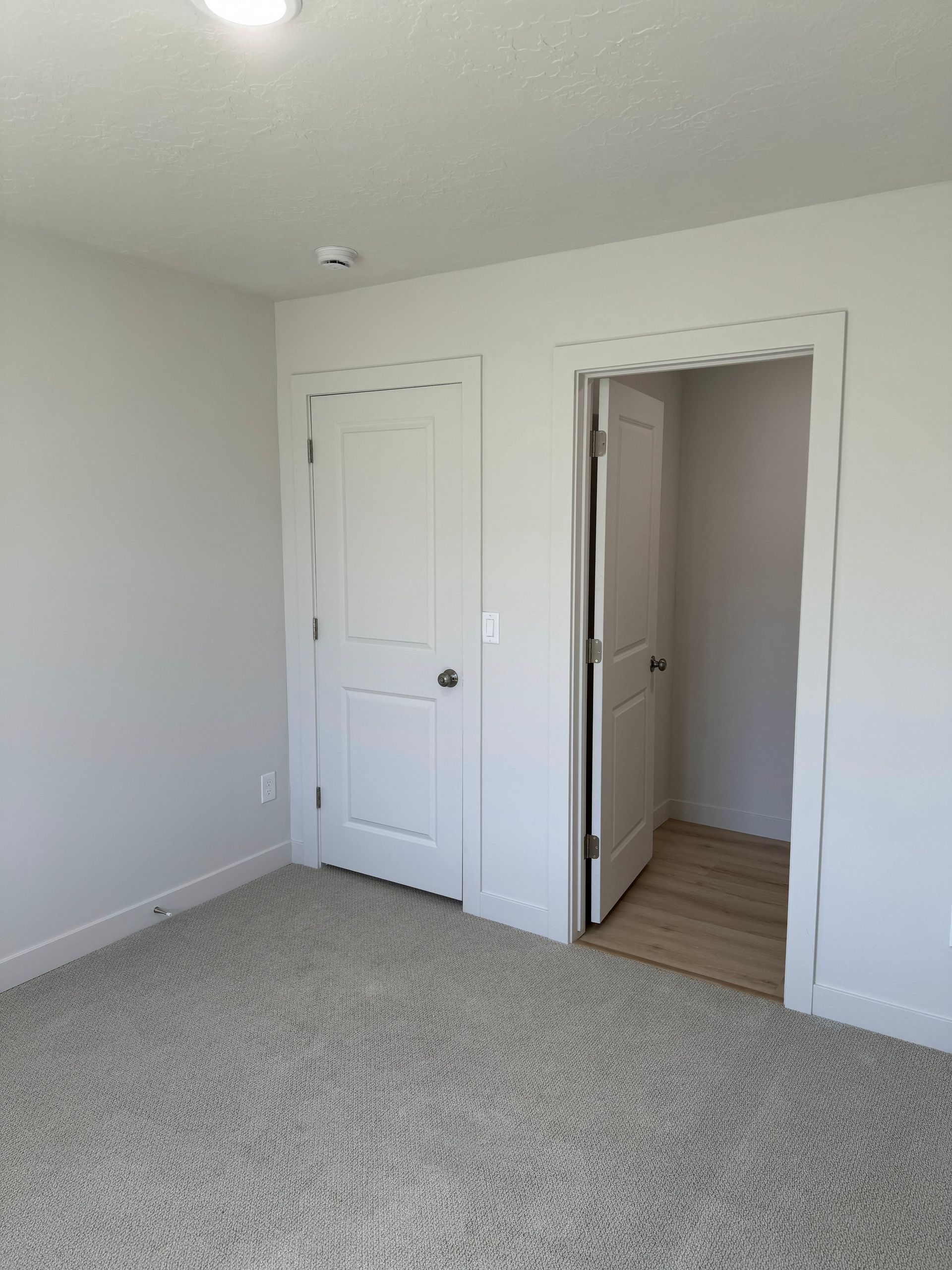 Empty white bedroom with carpet and two open doorways.