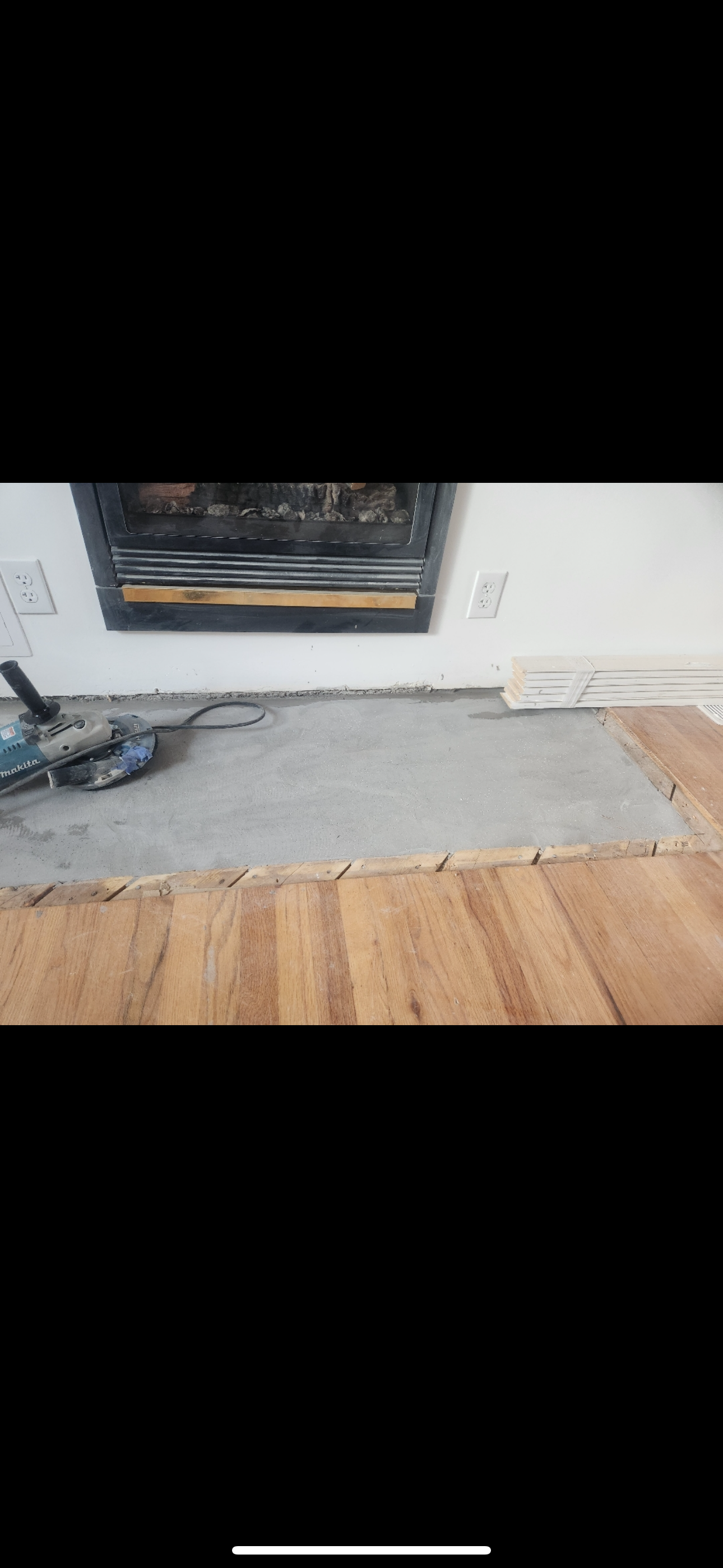 Partially removed carpet exposing wood floor beneath a wall-mounted fireplace and framed artwork