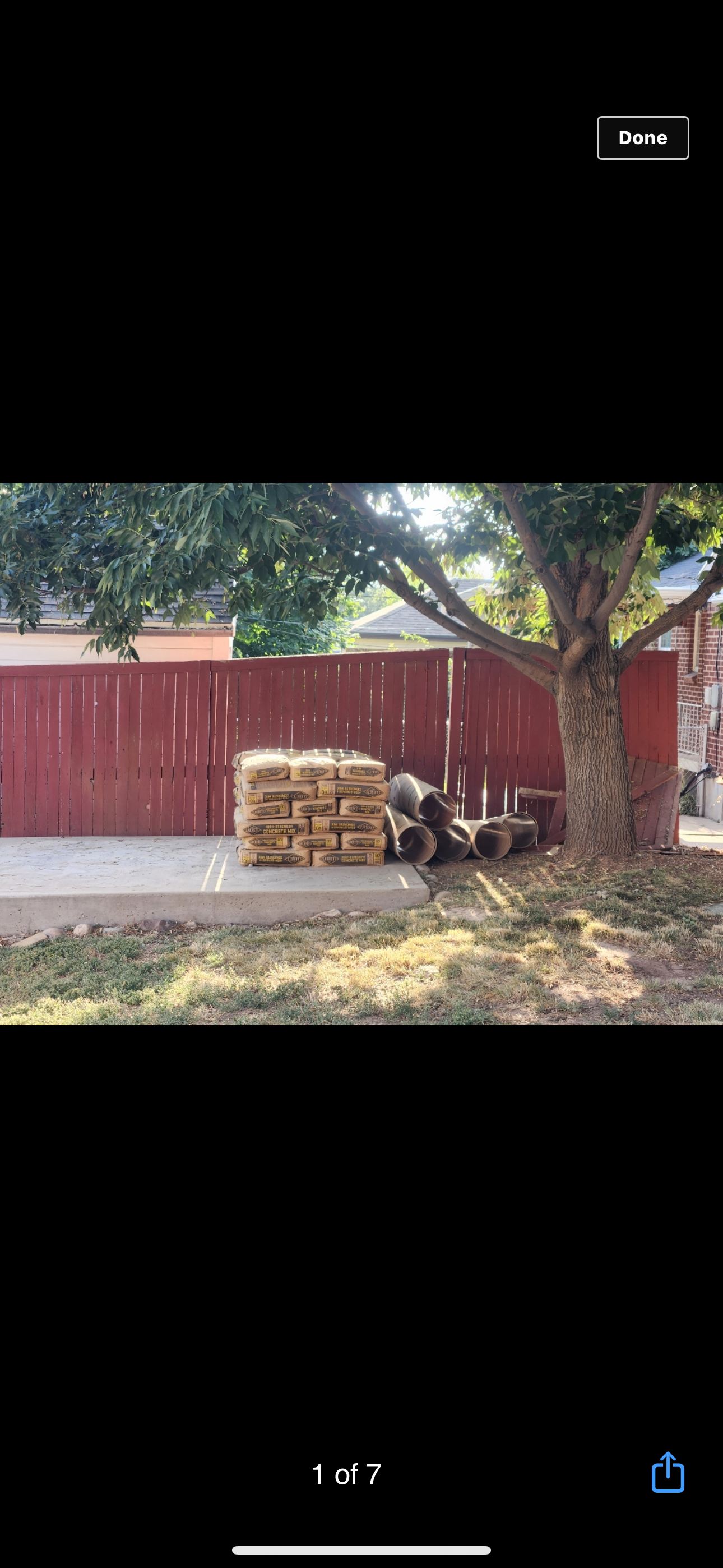 Backyard with stacked firewood by a red wooden fence under a tree.