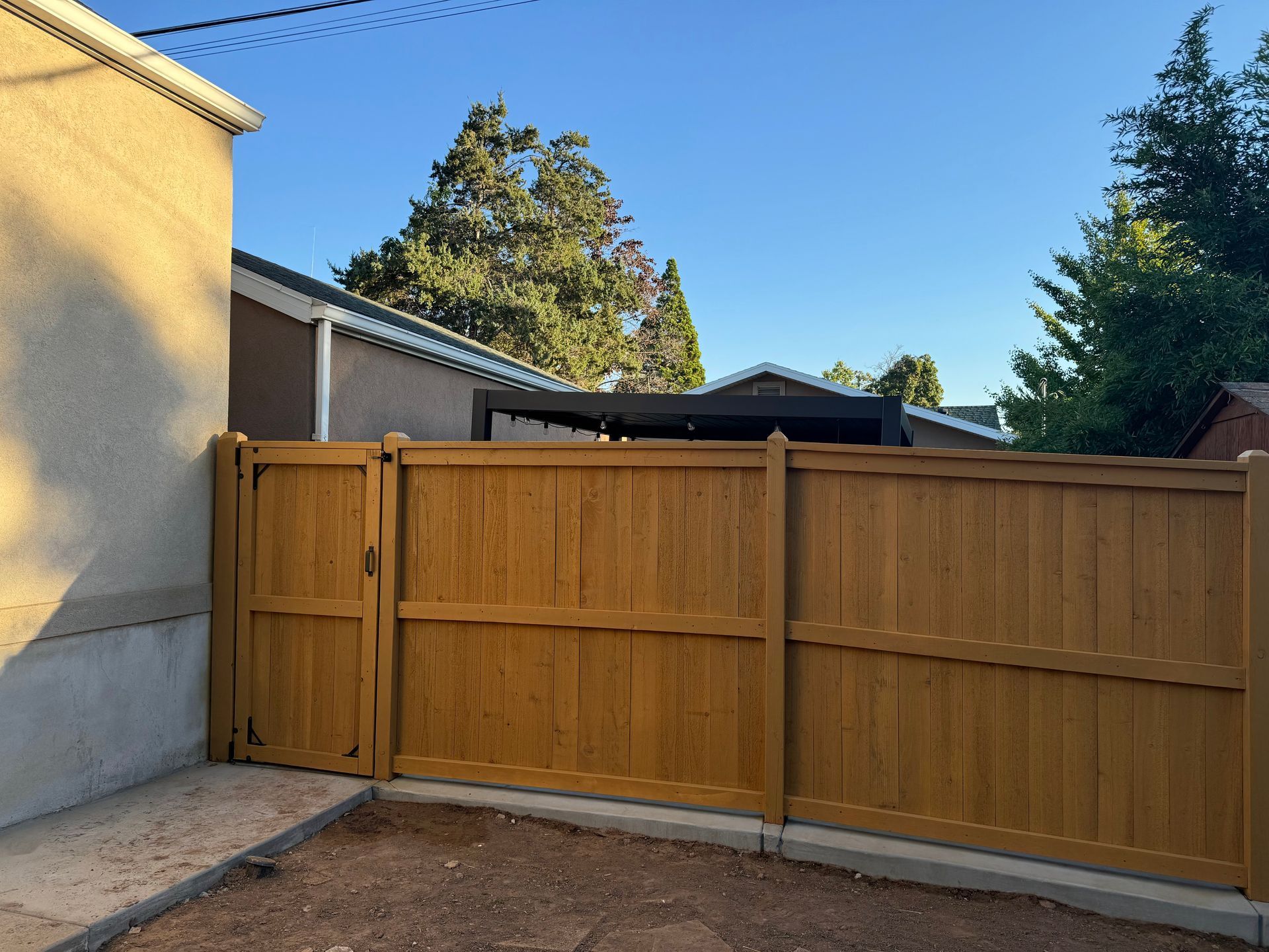 Wooden privacy fence and gate beside a beige house under a clear blue sky