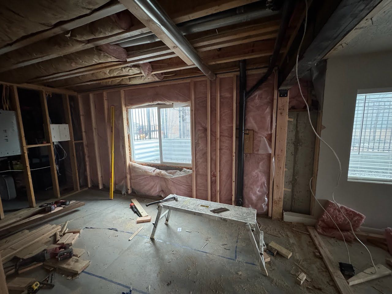 Bare unfinished room with exposed studs, debris on floor, and a window with blinds.
