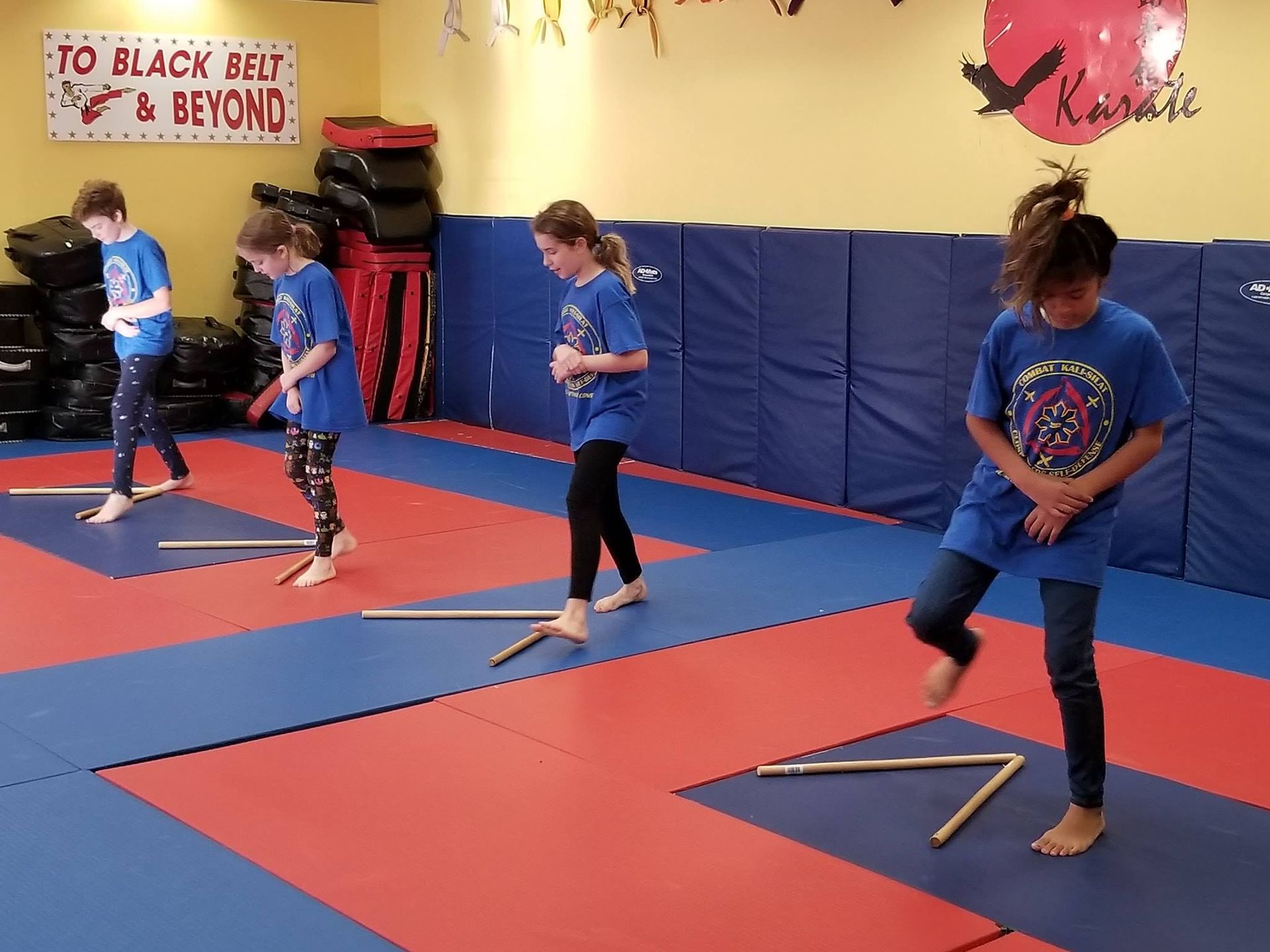 A group of kids are practicing karate in a gym with a sign that says to black belt & beyond