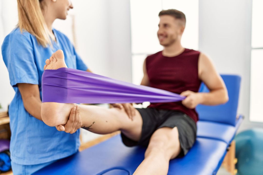 Un fisioterapista esegue esercizi di stretching sulla gamba di un paziente utilizzando una fascia elastica viola in una clinica.