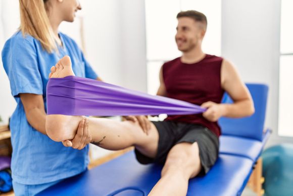Un fisioterapista esegue esercizi di stretching sulla gamba di un paziente utilizzando una fascia elastica viola in una clinica.