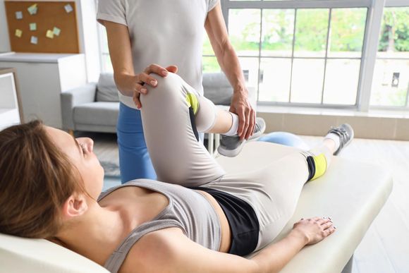 Un fisioterapista esegue esercizi di stretching sulla gamba di un paziente sdraiato su un lettino da trattamento in una luminosa stanza della clinica.