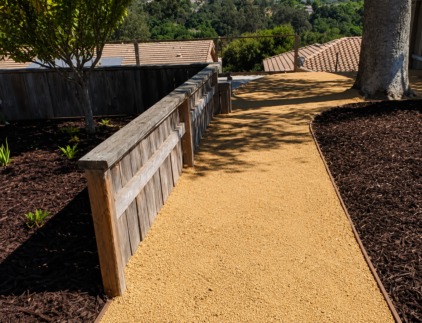 Gravel path beside a low wooden fence, bordered by mulch and trees in a landscaped garden.