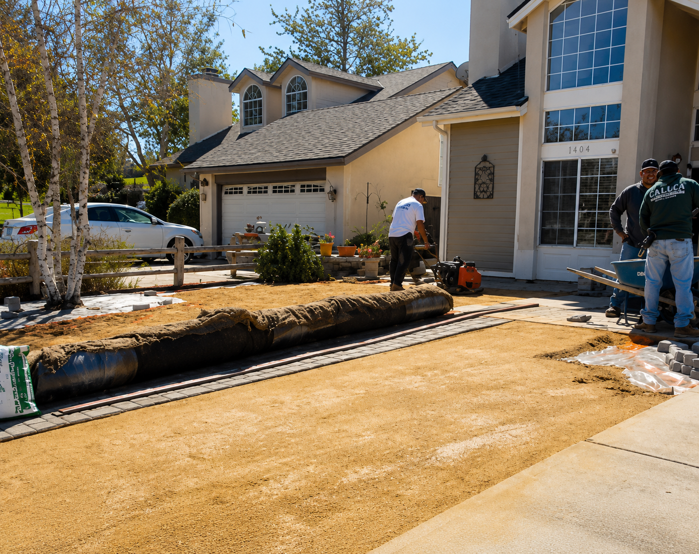 Workers installing new driveway paving beside a suburban house on a sunny day