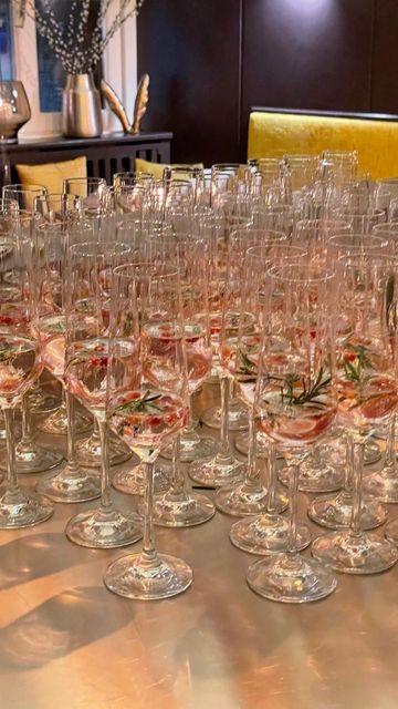 Auf einem Tisch standen Reihen von Champagnergläsern, gefüllt mit einem rosafarbenen Getränk und garniert mit einem Rosmarinzweig.