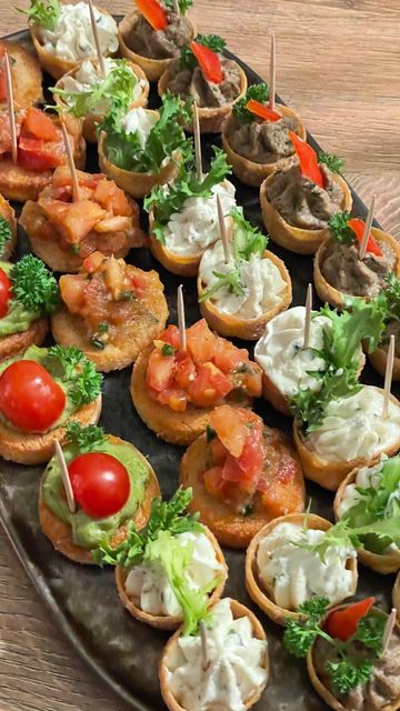 Eine silberne Platte gefüllt mit verschiedenen Appetithäppchen, garniert mit Sahne, frischem Grünzeug, Tomaten und herzhaften Aufstrichen.