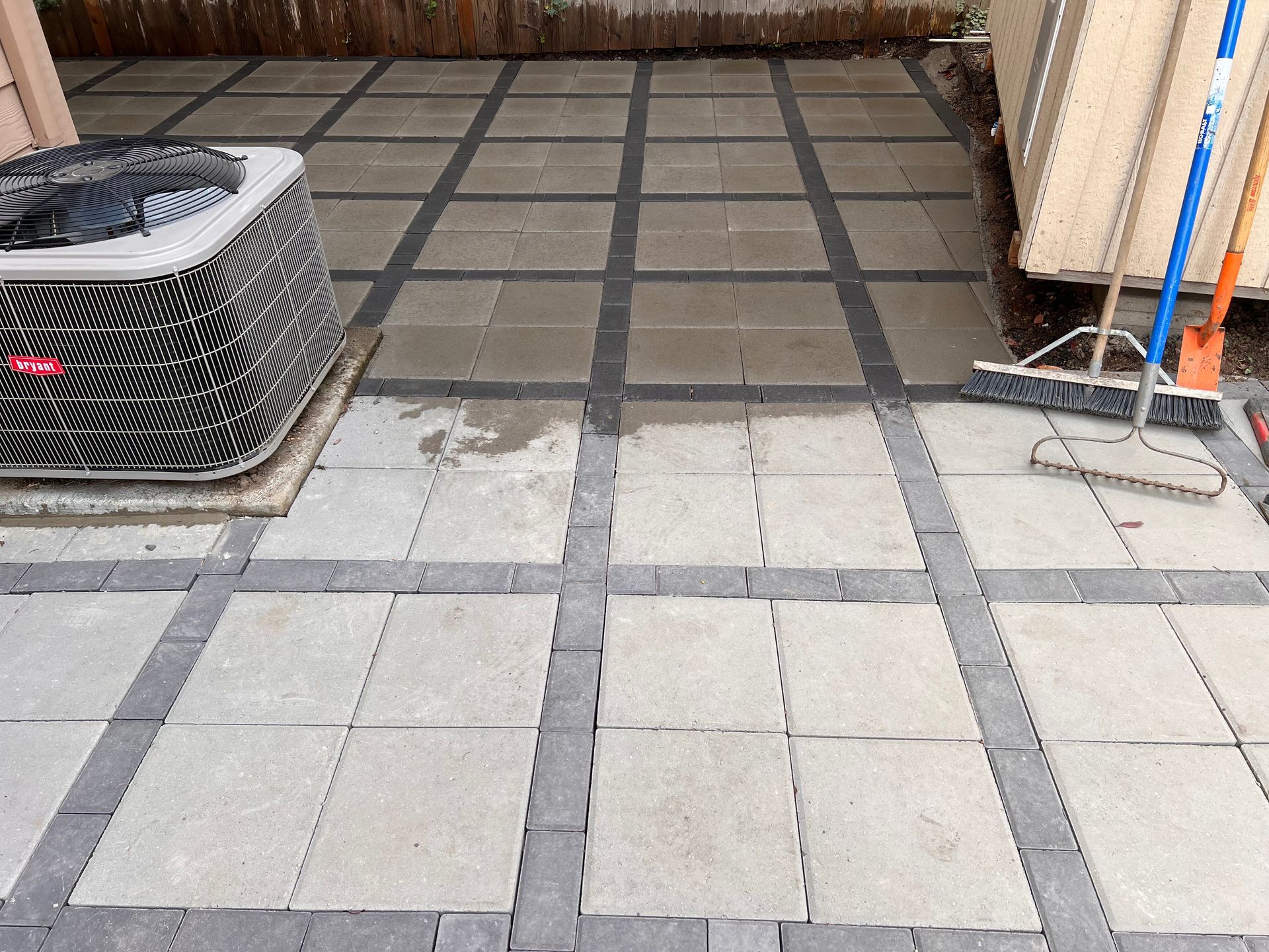 Patio paved with light grey and dark grey stones, with an AC unit on the left and cleaning supplies on the right.