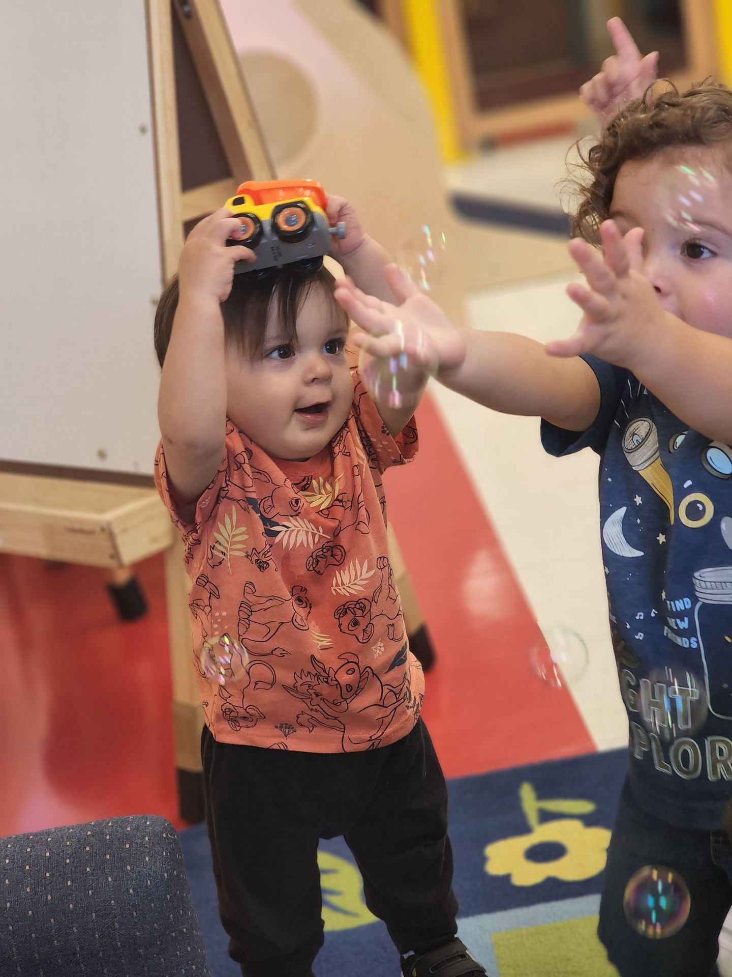 two toddlers are playing with bubbles and one is holding a toy car