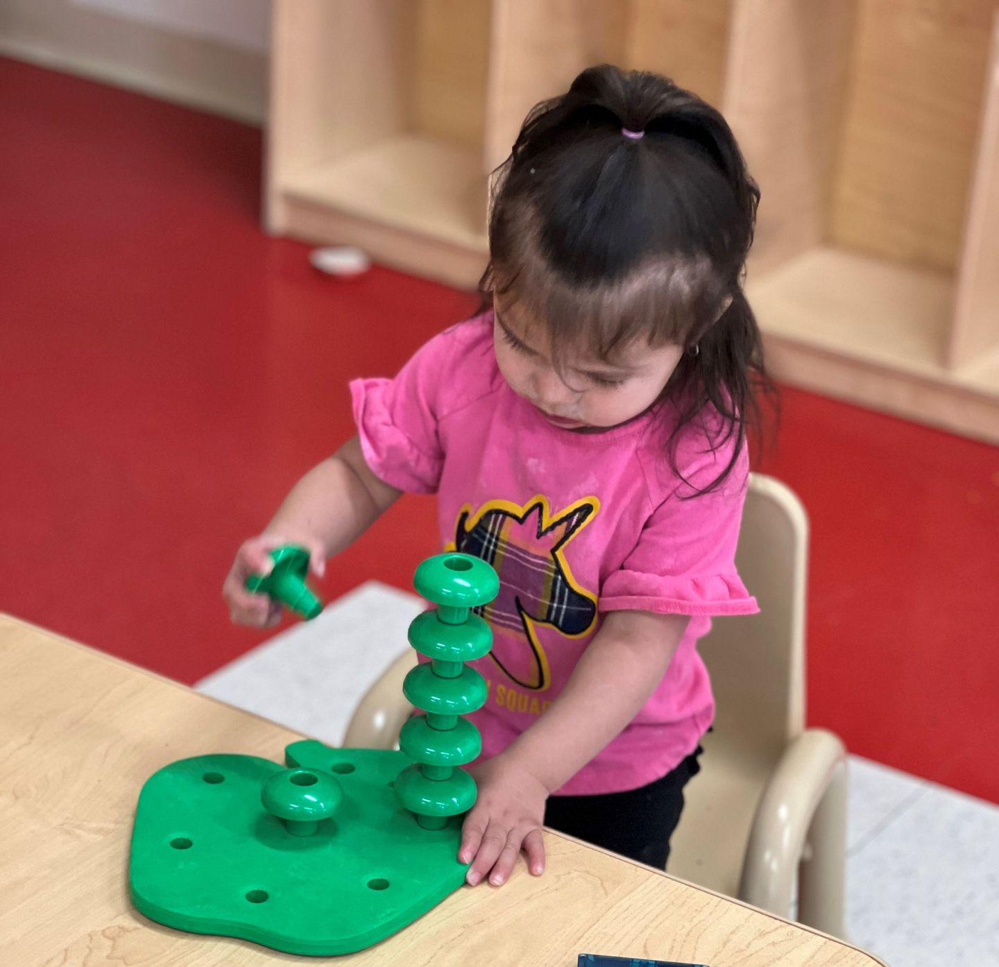 a little girl in a pink shirt is playing with a green toy