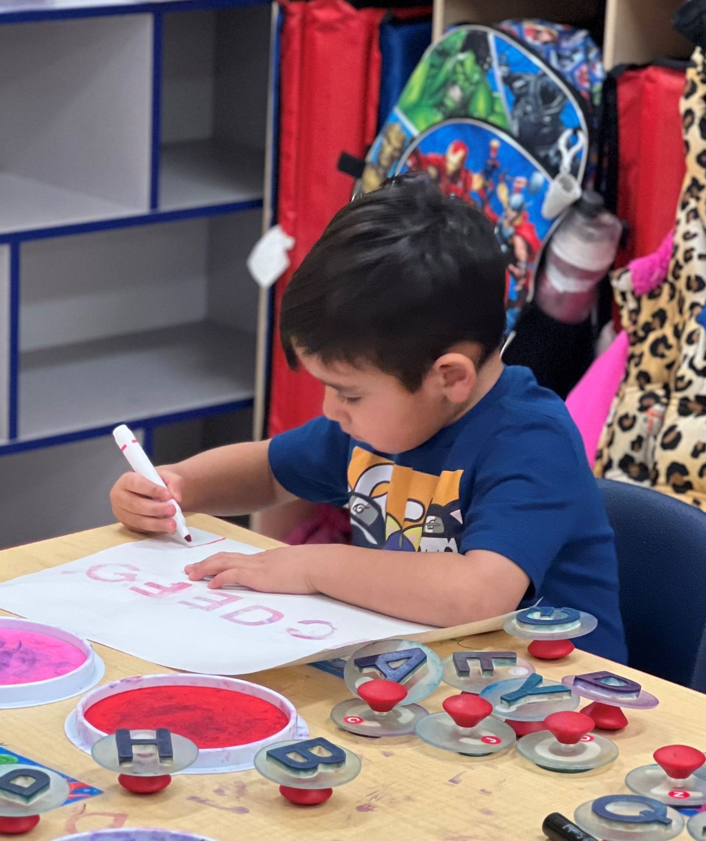 a young boy is sitting at a table writing on a piece of paper with a marker