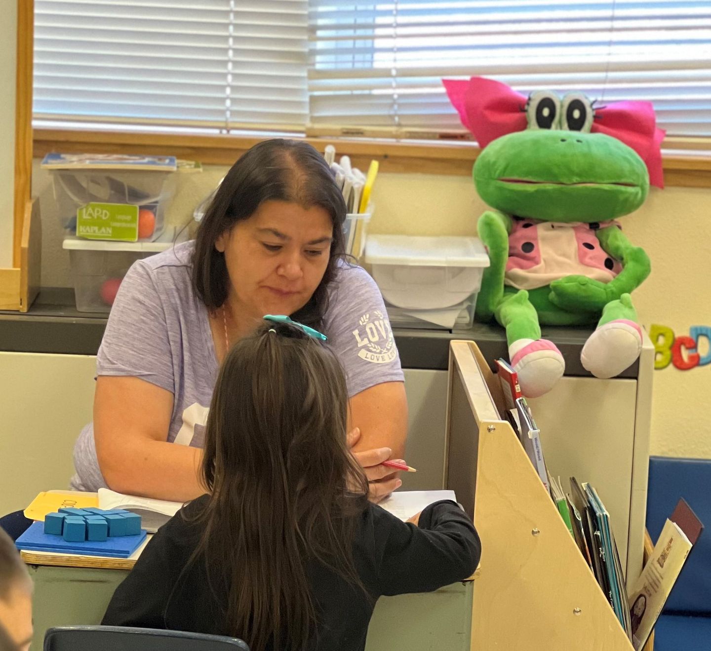 a woman is helping a little girl with her homework in a classroom