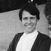 A man is smiling in a black and white photo while standing in front of a brick wall.