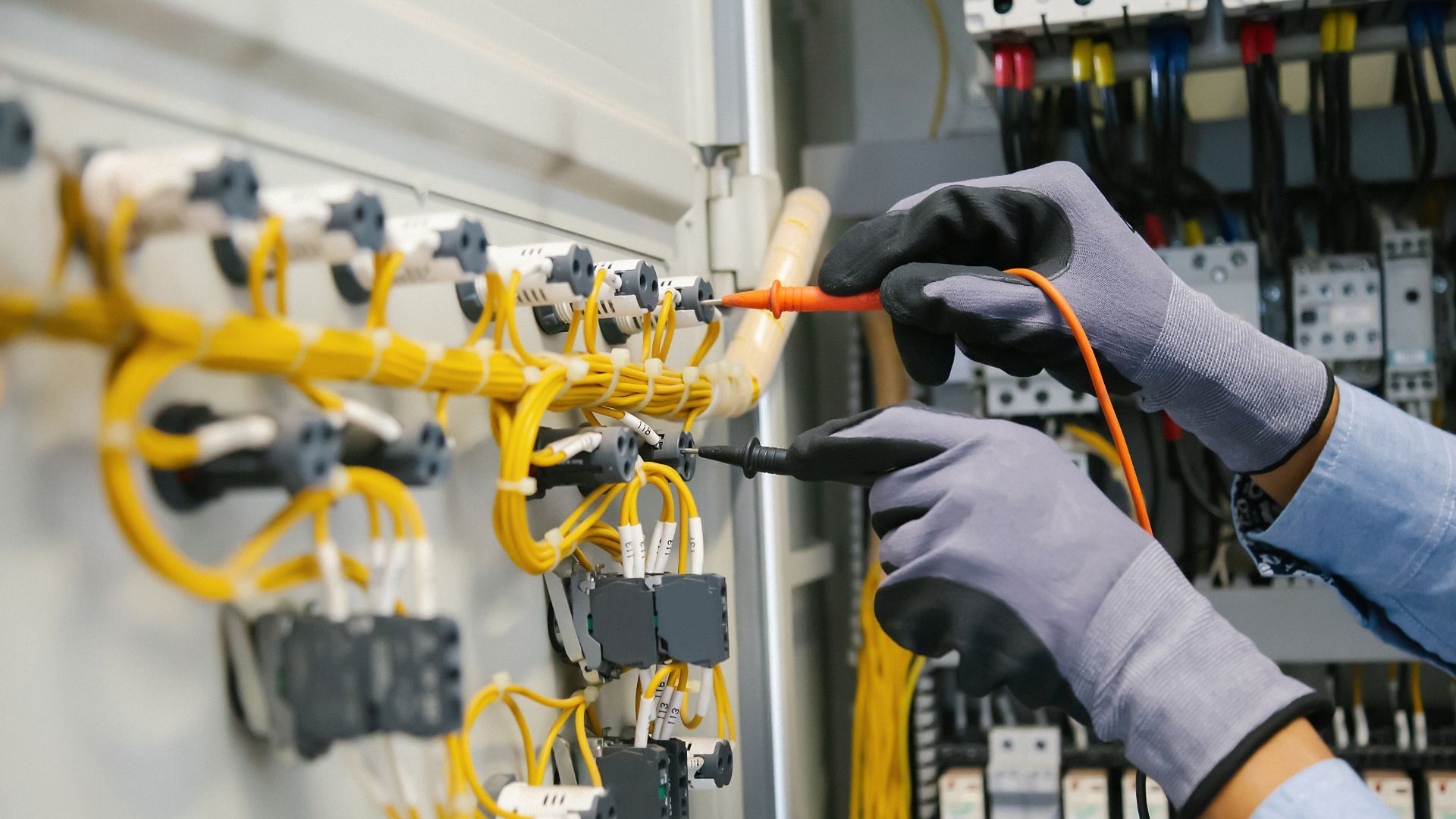 An electrician is working on a electrical panel with a multimeter.