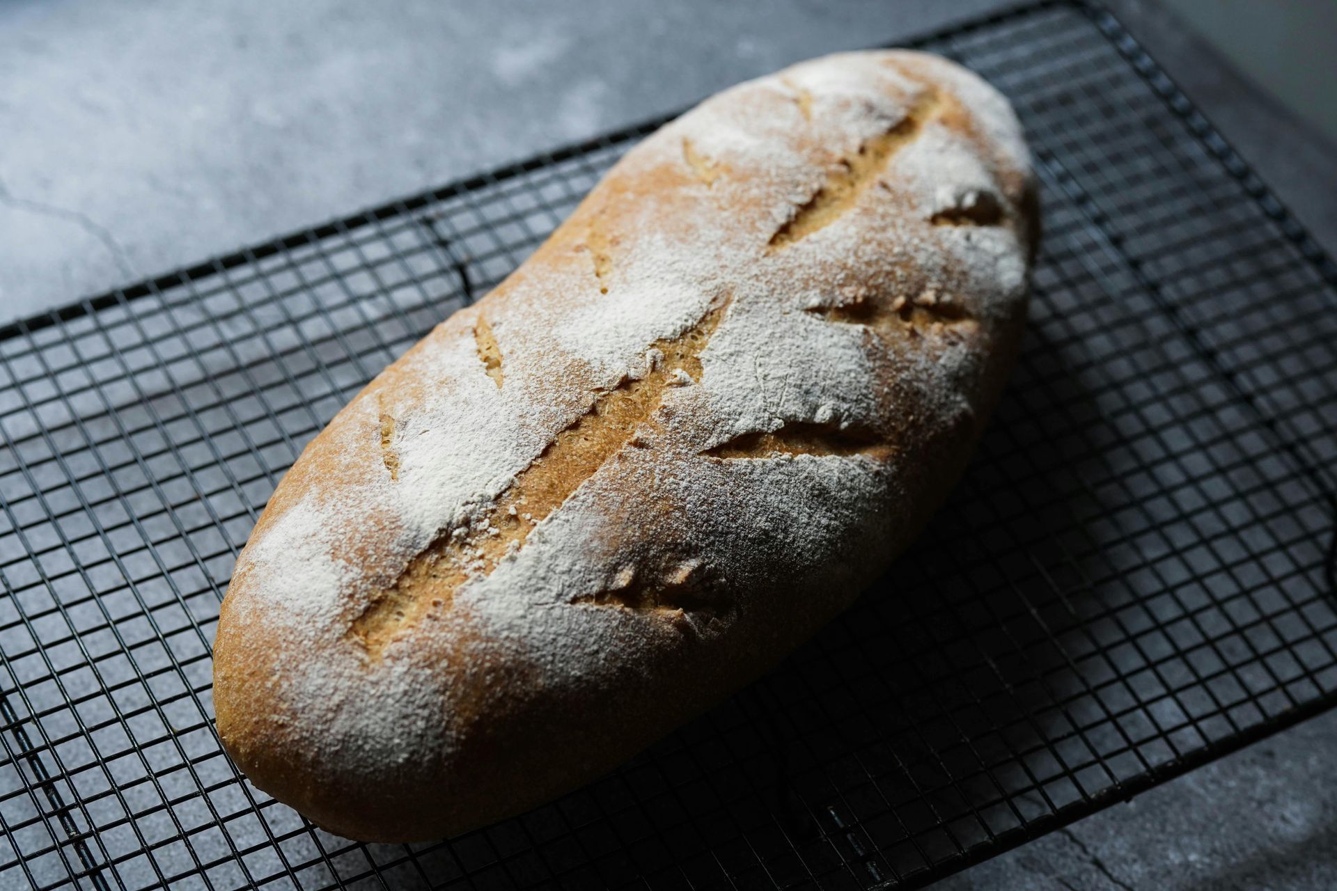 Loaf of bread with scored top dusted in flour, resting on a wire rack.