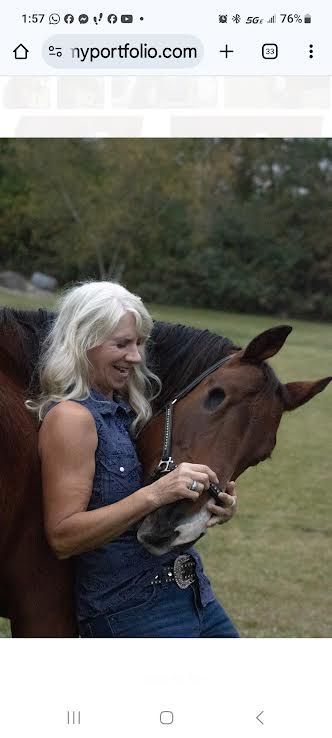 Smiling woman in denim vest petting a brown horse outdoors