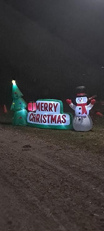 Christmas lawn display with glowing tree, “Merry Christmas” sign, and snowman at night