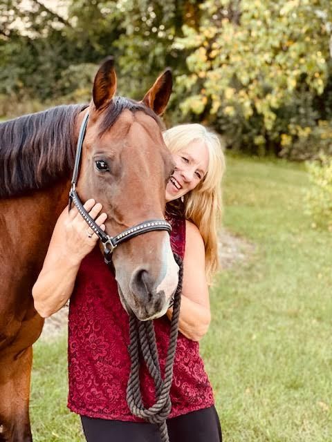 Woman hugging a brown horse outdoors, both facing the camera in a grassy yard.