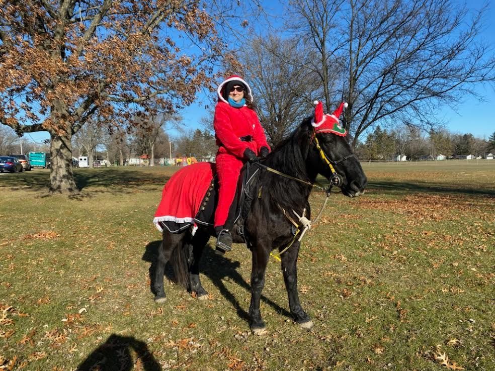 Person in a red Santa outfit riding a black horse in a park on a sunny day