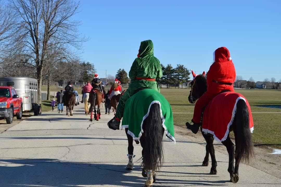 Two riders in green and red costumes ride horses down a sunny road during a parade