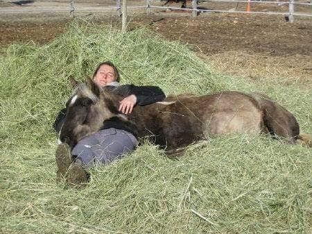 Person lying with a donkey on a hay pile outdoors.