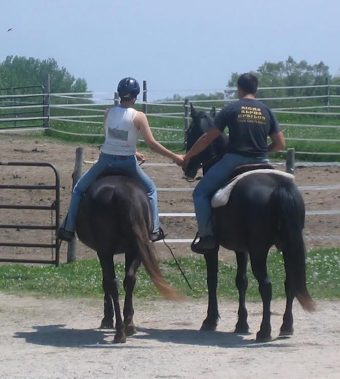 Two people on horseback in a fenced riding arena, viewed from behind.